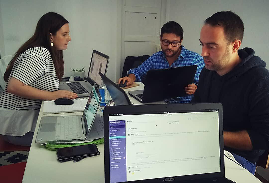 Coworkers de Espacio Arroelo trabajando con portátiles en mesa compartida; en pantalla, el Slack de la comunidad
