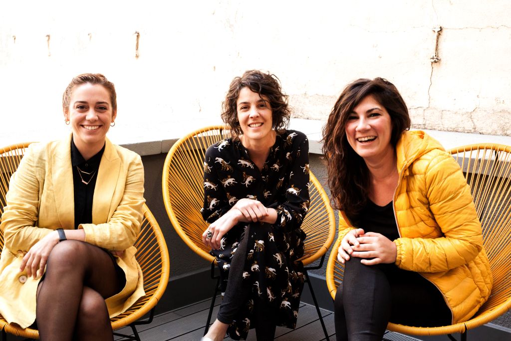 Tres mujeres emprendedoras de la comunidad Arroelo sonriendo en sillas Acapulco amarillas durante la Coworking Spain Conference
