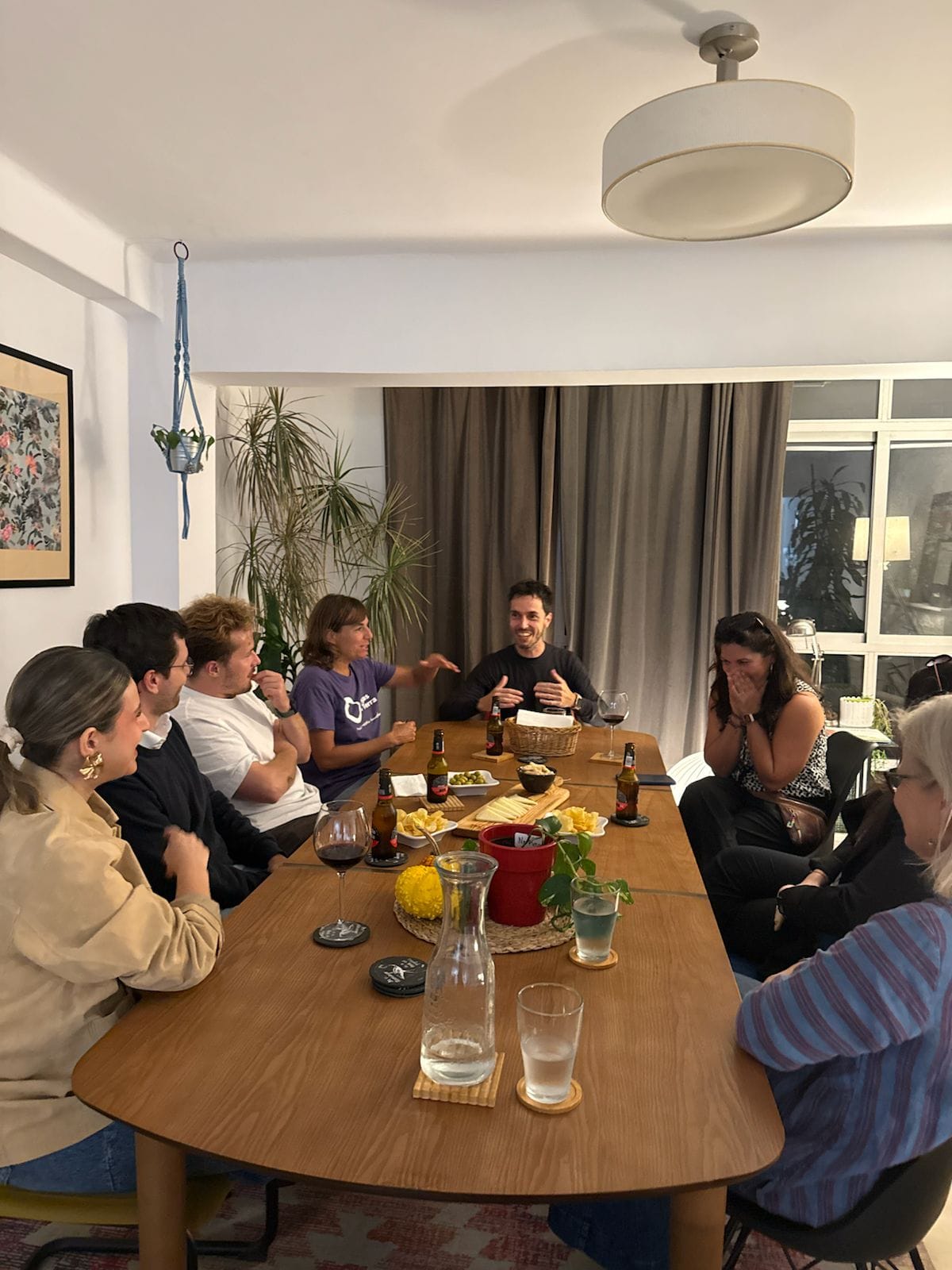 Personas alrededor de una mesa de madera en la Arroelada, con copas de vino, en el salón de Arroelo