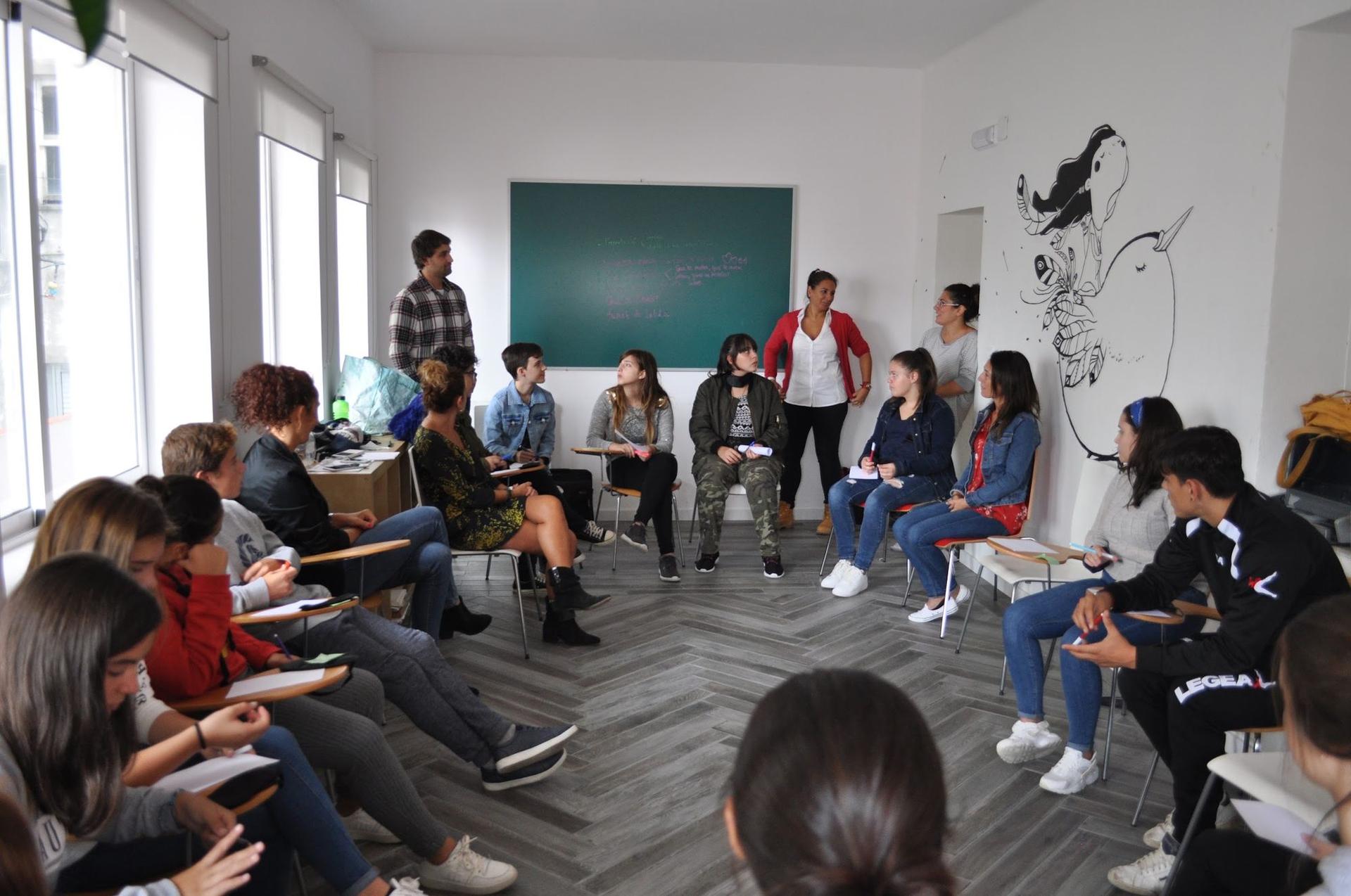 Taller en círculo: personas con cuadernos escuchan a una facilitadora junto a una pizarra