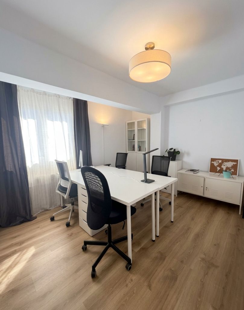 Sala XL con cuatro puestos enfrentados, sillas de malla, ventana con cortinas y mapa del mundo sobre taquillas blancas