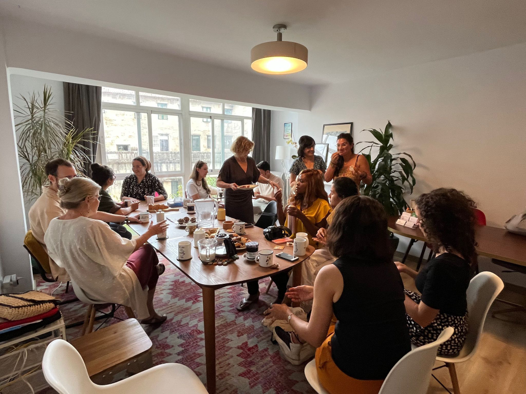 Un grupo diverso de personas compartiendo café y repostería en una gran mesa de madera en un espacio de coworking luminoso