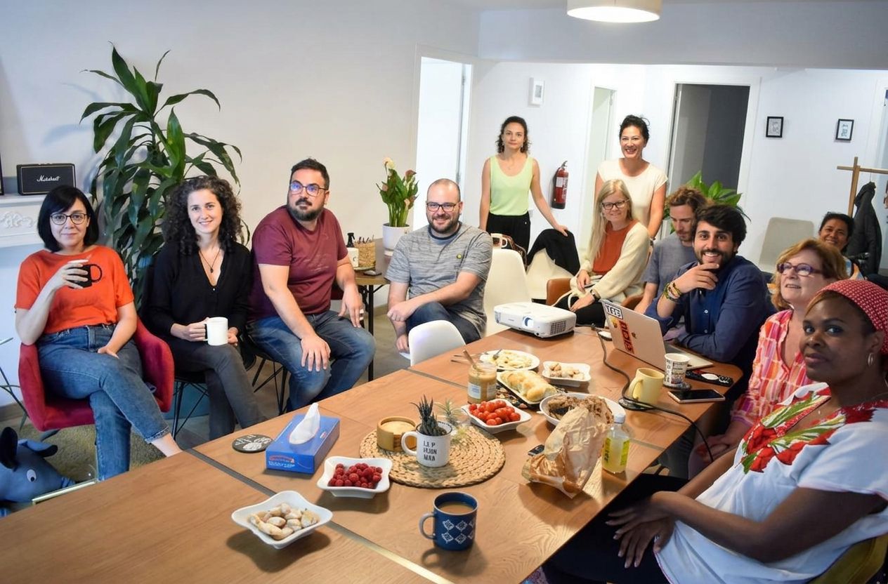 Grupo de la comunidad reunido alrededor de una mesa de madera con café, fruta y aperitivos en el salón