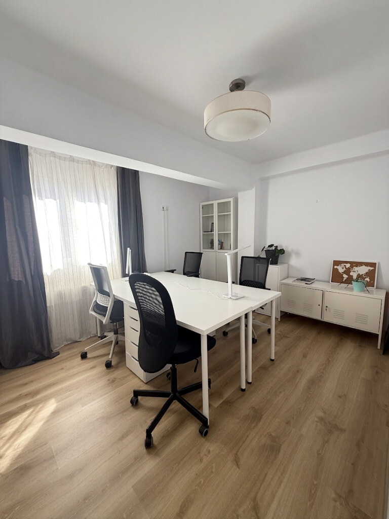 Sala exclusiva con cuatro puestos enfrentados, sillas de oficina, ventana con cortinas y estantería blanca