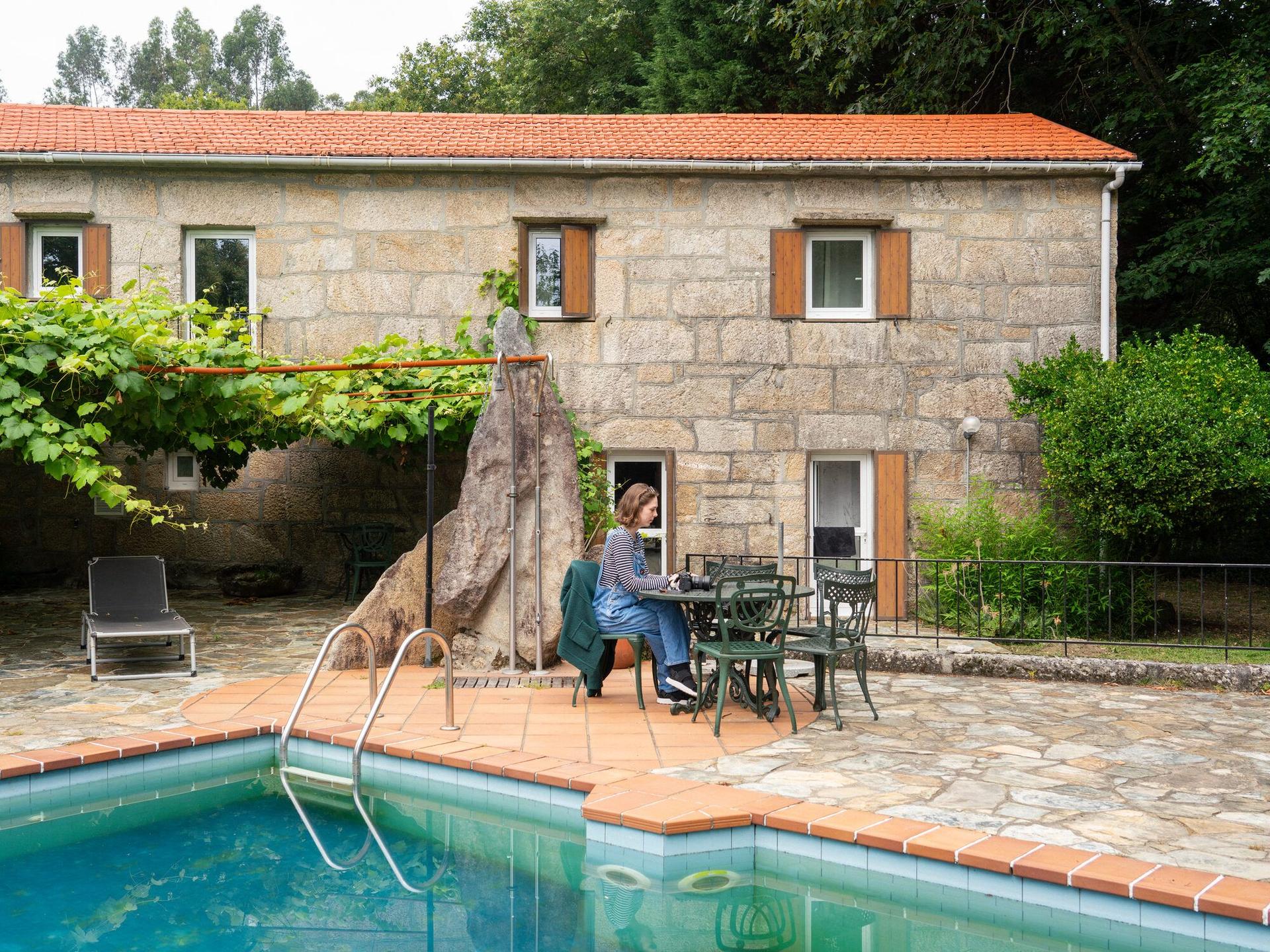 Coworker con portátil junto a la piscina turquesa de Anceu, en una casa de piedra rural