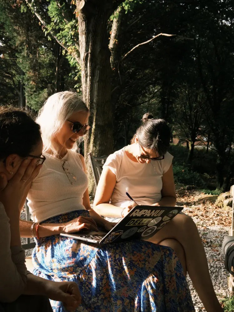 Tres compañeras trabajan juntas al aire libre en Anceu, con portátil bajo los árboles