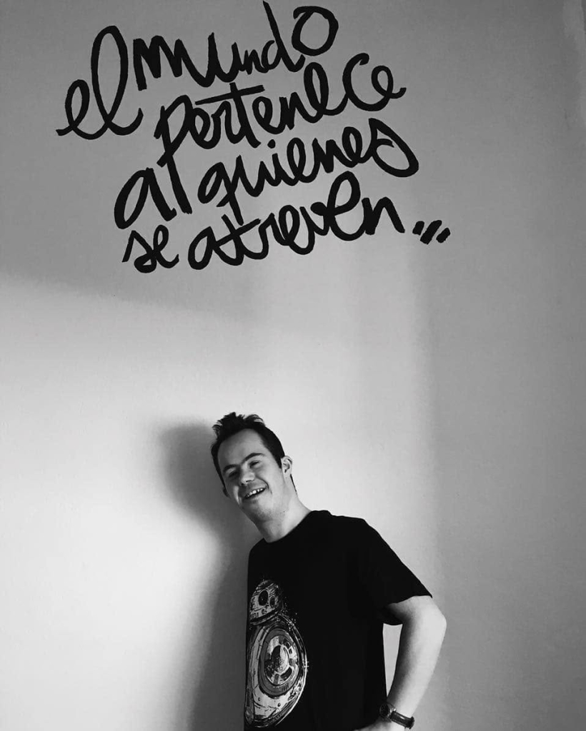 Celso, en blanco y negro, bajo el mural «el mundo pertenece a quienes se atreven...» en Espacio Arroelo