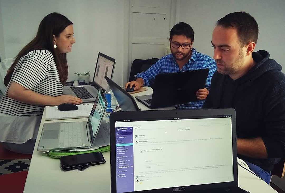 Coworkers de Espacio Arroelo trabajando con portátiles en mesa compartida; en pantalla, el Slack de la comunidad