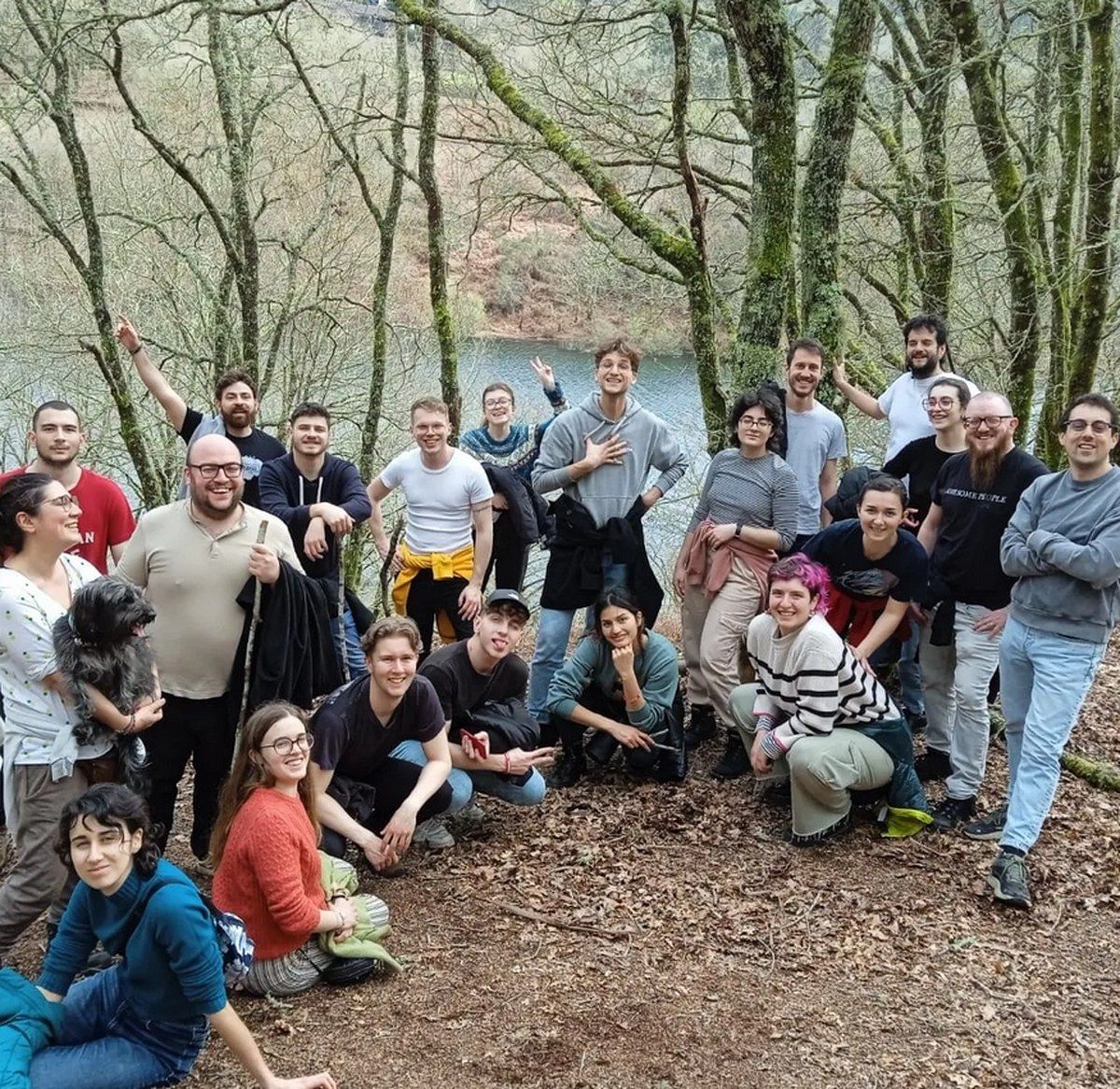 Grupo numeroso de personas posando con alegría en un claro del bosque junto al río