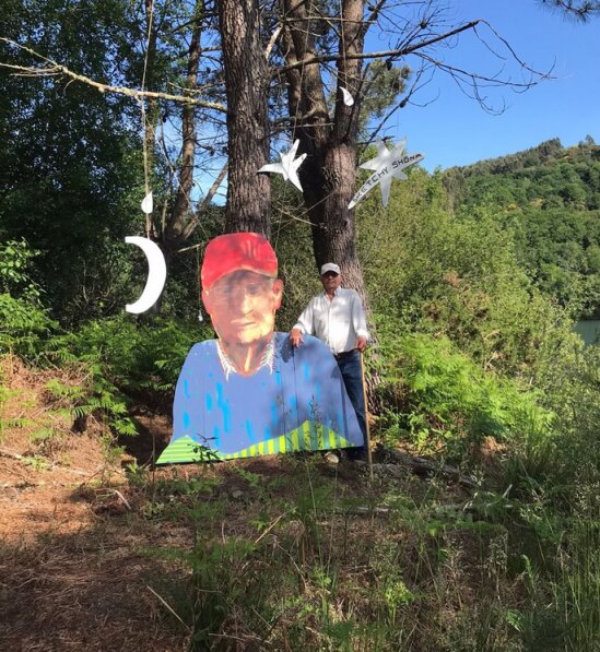 Persona con bastón junto a un gran retrato recortado al aire libre; Sketchy Shōna cuelga entre los pinos